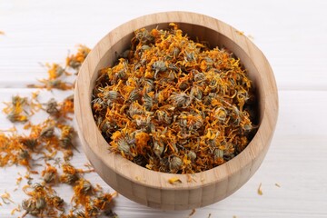 Dry calendula flowers in bowl on white wooden table, closeup