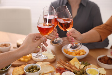 People clinking glasses with rose wine above table indoors, closeup