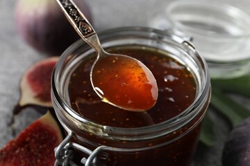 Spoon with tasty sweet jam over jar and fresh figs on table, closeup