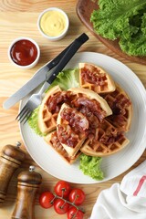 Tasty Belgian waffles served with bacon, lettuce and sauces on wooden table, flat lay