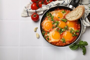 Delicious Shakshuka in frying pan served on white tiled table, flat lay. Space for text