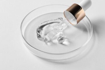 Petri dish with sample of cosmetic serum and pipette on white background, closeup