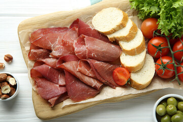 Board with delicious bresaola served with different snacks on white wooden table, flat lay
