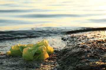 Used plastic bag near water at beach, space for text. Environment pollution