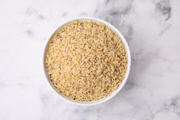 Raw bulgur in bowl on marble table, top view