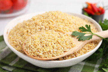 Bowl and spoon with raw bulgur on table, closeup