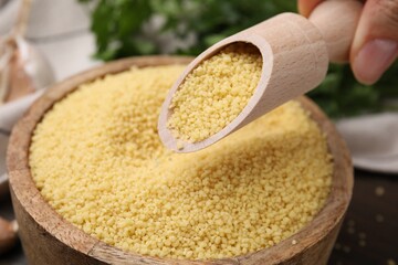Taking raw couscous with scoop from bowl, closeup