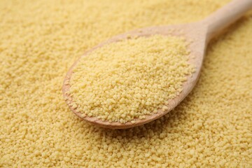 Wooden spoon and uncooked organic couscous as background, closeup