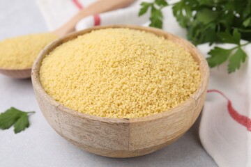 Raw couscous in wooden bowl on table, closeup