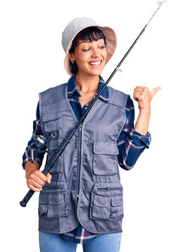 Young brunette woman with short hair wearing fisherman equipment pointing thumb up to the side smiling happy with open mouth