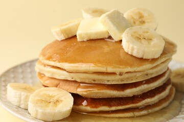 Delicious pancakes with bananas, honey and butter on beige background, closeup