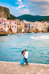 a couple of men and woman hugging at the waterfront on vacation in Sicily visiting the old town of Cefalu, sunset at the beach of Cefalu Sicily, the old town of Cefalu Sicilia Italy
