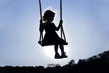 a silhouette of a little girl on a swing with a clear sky as a background