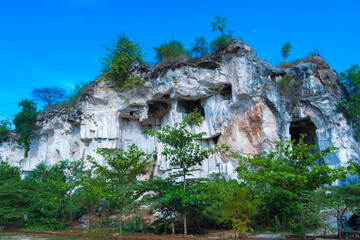 A weathered limestone cliff, adorned with a smattering of trees, stands tall against a clear blue sky in Setigi, Gresik, East Java, Indonesia.