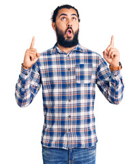 Young arab man wearing casual clothes amazed and surprised looking up and pointing with fingers and raised arms.