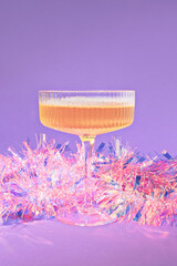 A Holiday Champagne Cocktail Wrapped in Pink Iridescent Tinsel Christmas Decoration on a Purple...