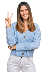 Young woman wearing casual clothes smiling looking to the camera showing fingers doing victory...