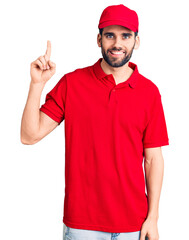 Young handsome man with beard wearing delivery uniform showing and pointing up with finger number one while smiling confident and happy.