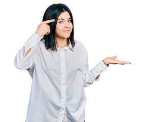 Young brunette woman with blue eyes wearing oversize white shirt confused and annoyed with open palm showing copy space and pointing finger to forehead. think about it.