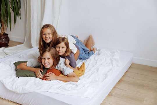Three sisters play and fool around on the bed in casual clothes against a white wall. High quality photo