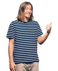 Handsome caucasian man with long hair wearing casual striped t-shirt smiling with happy face looking and pointing to the side with thumb up.