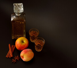 Apple-peach liqueur with cinnamon and anise on a black background, homemade alcohol in a decanter and two glasses next to ripe fruit.