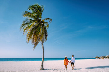 Eagle Beach Aruba with Palm Trees on the shoreline of Eagle Beach in Aruba, a couple man, and woman on the beach of Aruba during vacation at sunset