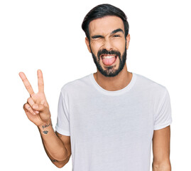Young hispanic man wearing casual white t shirt smiling with happy face winking at the camera doing...