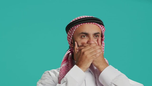 Muslim guy covers eyes, ears and mouth on camera, showing three wise monkeys metaphor symbol. Middle eastern person creating dont hear, see or speak concept sign, islamic attire.