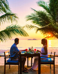 couple having a romantic dinner on the beach of Koh Chang Thailand during sunset, men and woman...