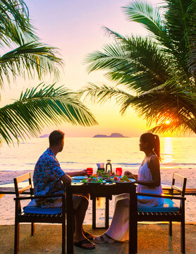 couple having a romantic dinner on the beach of Koh Chang Thailand during sunset, men and woman dinner on the beach at sunset with palm trees at a luxury resort during vacation honeymoon