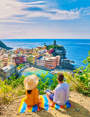 A couple of caucasian men and Asian women are on the hill looking out over the bay of Vernazza...