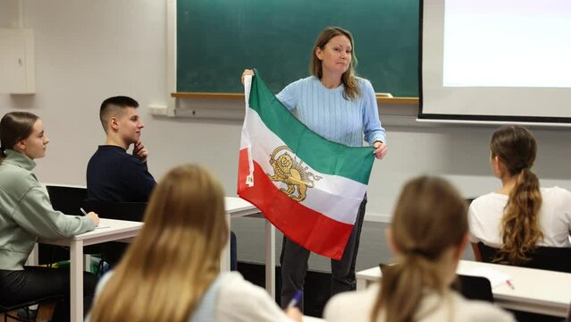 Adult female teacher showing Iranian flag to students. High quality 4k footage
