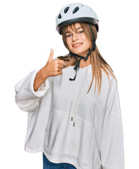 Teenager caucasian girl wearing bike helmet doing happy thumbs up gesture with hand. approving expression looking at the camera showing success.