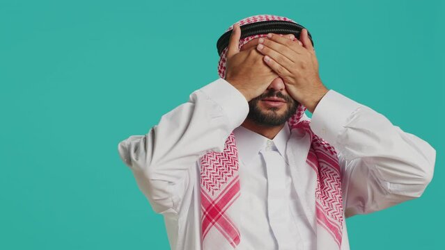 Arab person covers eyes, ears and mouth in studio, presenting three wise monkeys metaphor sign. Middle eastern adult showcasing dont hear, see or speak symbol, muslim costume.