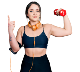 Young hispanic girl wearing sportswear using dumbbell smiling happy pointing with hand and finger to the side