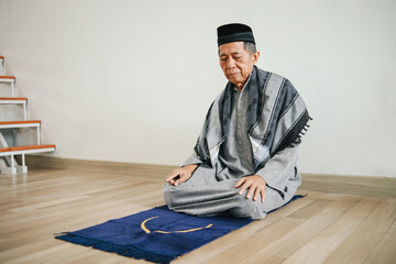 Senior Asian Muslim man praying on prayer mat and doing last movement in salat procedure. The...