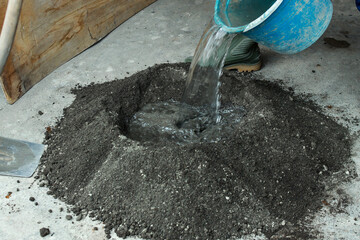 Water pouring into a mixture of cement and sand. A process of mixing cement at a construction site. - obrazy, fototapety, plakaty