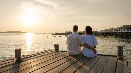 couple sitting on a wooden deck pier in the ocean during sunset in Samaesan Thailand