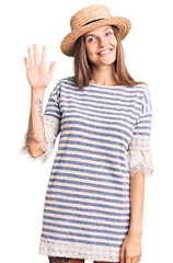 Beautiful caucasian woman wearing summer hat showing and pointing up with fingers number five while smiling confident and happy.