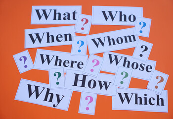 Paper cards with Wh-question words and question marks on orange background. Concept. Teaching aid. Education materials for teach WH- question. Asking questions. Suspicious symbol to find answer.     