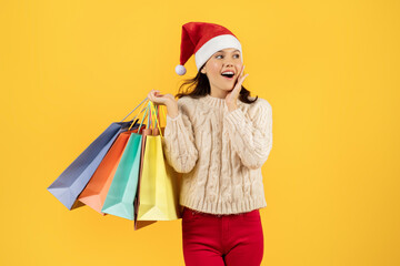 lady shopper in Santa hat holding shopping bags, yellow backdrop