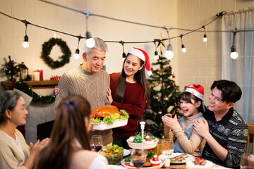 Asian senior father and daughter serving roasted turkey food on dinner table while warm family gathering and clapping hand for greeting welcome to Happy Christmas Eve party in the living room house