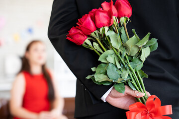 Asian gentle boyfriend hiding diamond ring and red roses bouquet behind back prepare for surprise...
