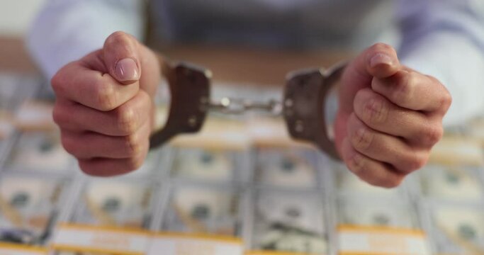 Woman hands in handcuffs lie on pile of dollar bills