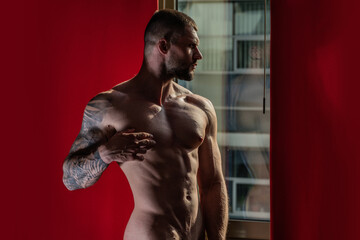 Sensual muscular hunk in room on window curtains. Muscular shirtless man model in bedroom. Gay sexy...