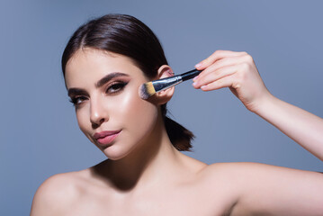 Obraz premium Powder brush. Girl hold blusher, apply powder visage with brush, isolated studio background. Young woman powdering cheeks. Makeup brush. Female model gets blush powder with brush.