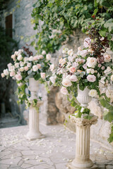 Wedding semi-arch of bouquets of flowers on pedestals near a stone wall in the garden