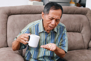 Asian elderly man hold vitamin pills and glass of natural clean water. Painful old age and daily...