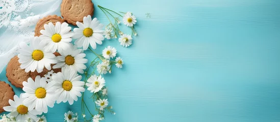 Tuinposter A biscuit with chamomile flowers on parchment in the frame. Turquoise tablecloth with daisies on the table. © 2rogan